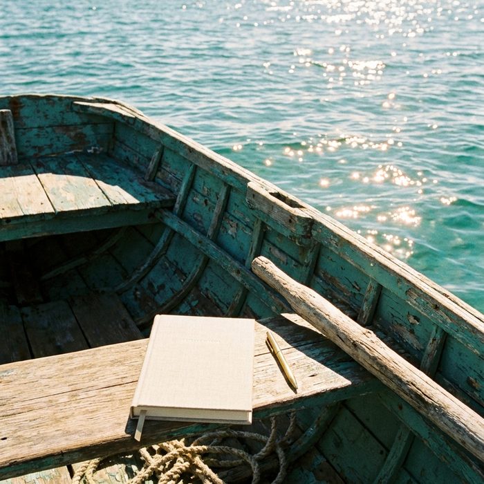 Claude für dein Business: Notizbuch auf der Bank eines alten Holzboots im türkisen Wasser